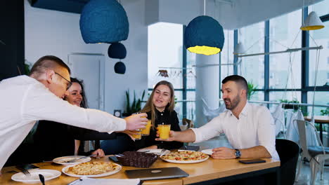 company of mid-aged people gathered at the dining table. people drink orange juice and going to have pizza. office lunch at work.