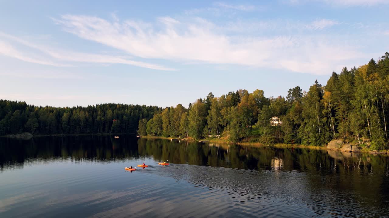 Three kayakers paddle through a calm forest lake in Norway during golden hour
