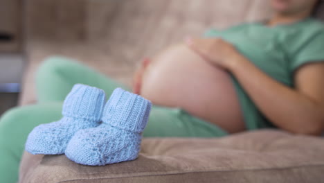 beautiful knitted socks for future baby. new blue socks on blur background of expectant mother lying on a sofa. pregnancy time.