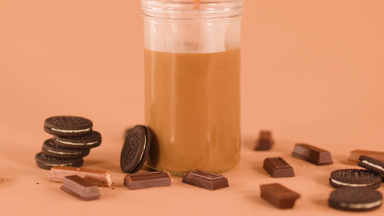 Chocolate beverage poured into glass jar, surrounded by cookies and chocolate bars, warm studio lighting