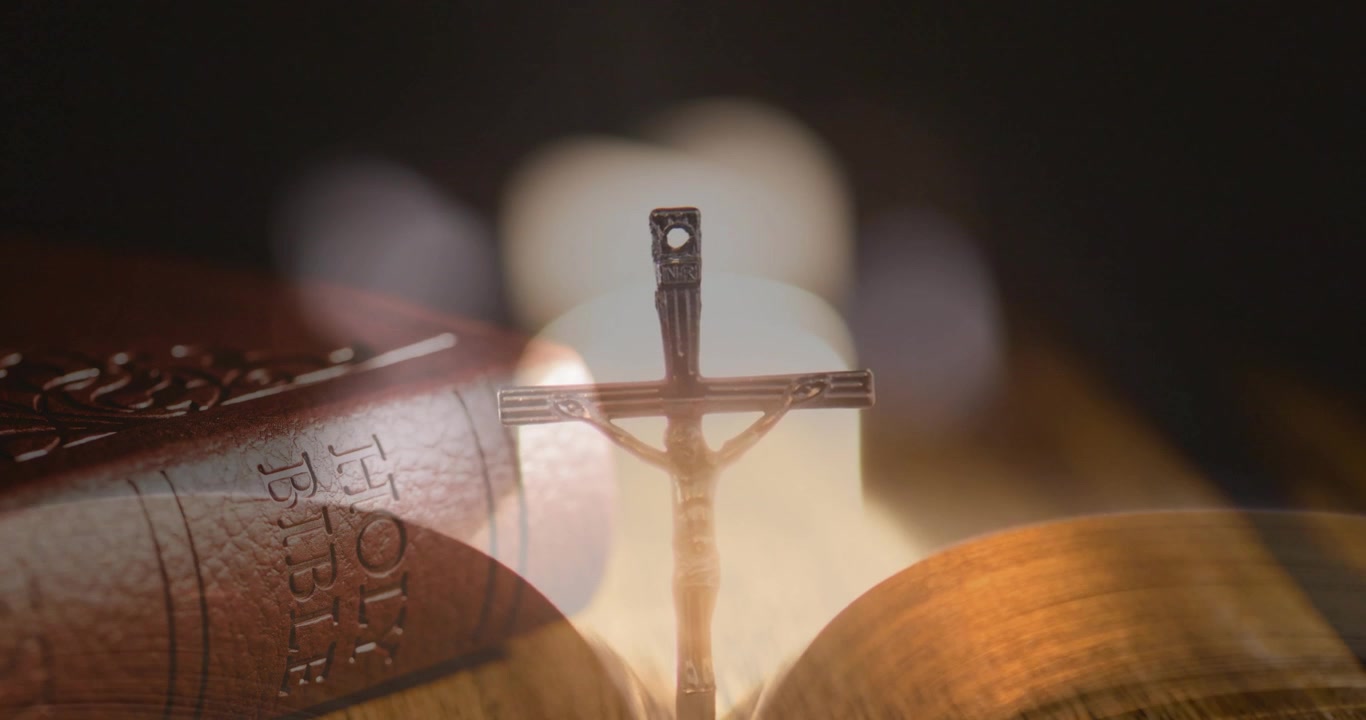 Crocifisso che appare e si innalza con effetto bokeh fiorito, la telecamera mette a fuoco pagine che si sfogliano incorniciando la Sacra Bibbia.