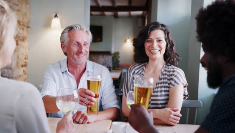 senior white man and hispanic woman sitting at a table in a pub making a toast with colleagues, close up, over shoulder view