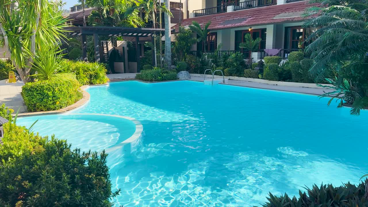 Et vidvinkelbillede af en lys turkis swimmingpool omgivet af frodigt tropisk grønt.
