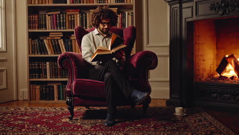 man reading by the fireplace in a cozy library