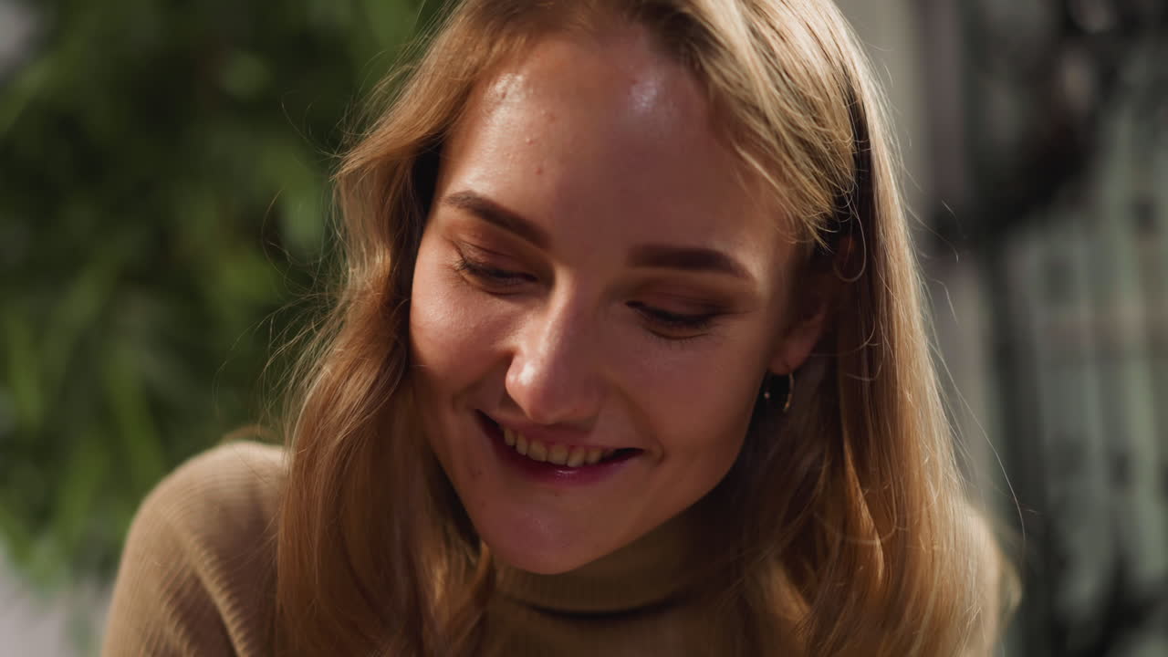 Pěkná žena s dlouhými rozpuštěnými světlými vlasy se usmívá ve světlé místnosti.