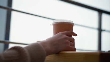 close-up of woman hand tapping beverage cup on wooden table with blurred background, soft light creating peaceful and focused ambiance, elegant interaction with coffee in modern cafe setting