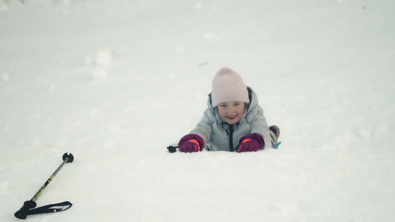 niña sonriente en abrigo de invierno se desliza por el banco de nieve en el vientre