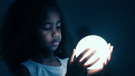 young girl holding a glowing sphere in a dark room