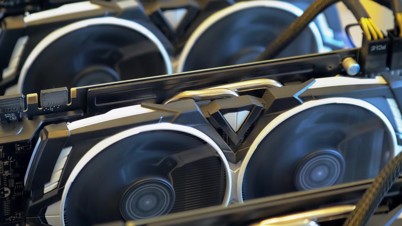 Primo piano diagonale mostra diverse schede grafiche in funzione con veloci doppie ventole, tubi di calore in metallo e un cavo di alimentazione intrecciato che attraversa un impianto di mining GPU aperto