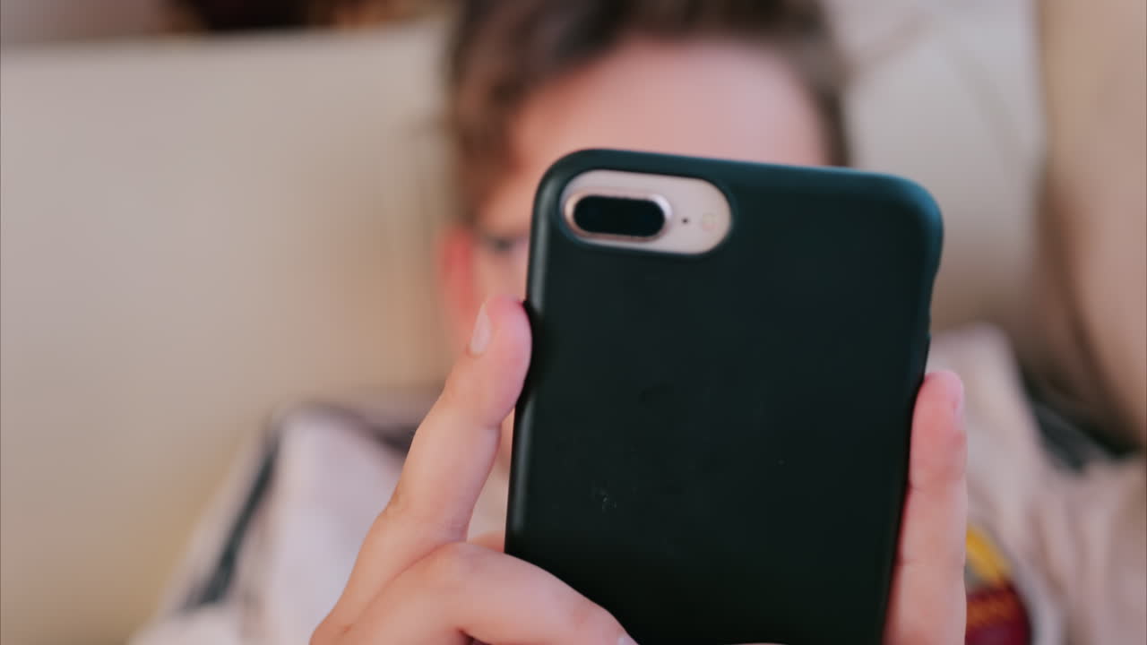 Close up of a child holding a smartphone with a black case while lying down indoors