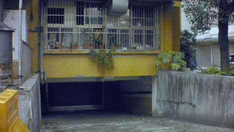 노란색 타일로 된 벽이 있는 2층 높이 건물인 더러운 창 굴뚝 구조처럼 빈민가까지 폐쇄된 금속 문이 있는 더러운 오래된 시멘트 포장 지하 차고에서 수직으로 올려다보는 전망