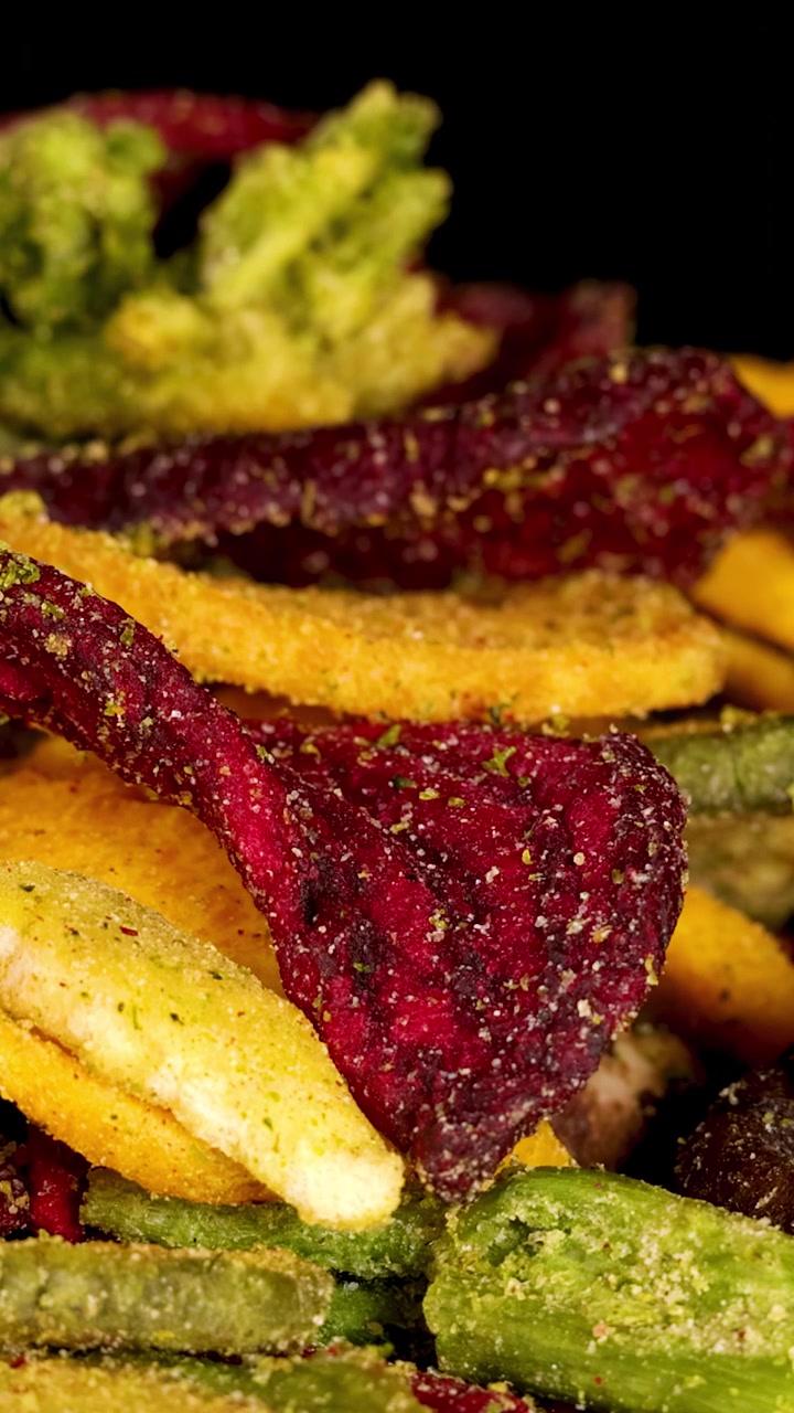 Vista macro rotante di chips assortite di barbabietola, fungo e ortaggi a radice essiccati sotto illuminazione da studio.
