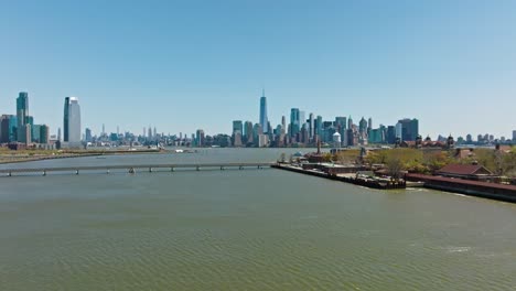 aerial establishing drone shot of manhattan skyline with one world trade center and bridge connecting to ellis island in foreground - new york city in summer season