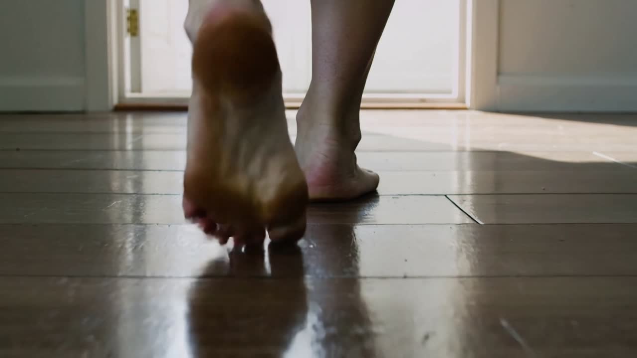 Film subject walking toward doorway across glossy floor, initial heel lift causing heel-toe steps