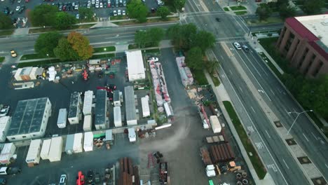 Construction-site-salt-lake-city,utah,-united-states-on-sunrise-at-7AM-in-summer-with-green-trees,-containers-and-heavy-equipment-on-ground,-few-cars-drive-by