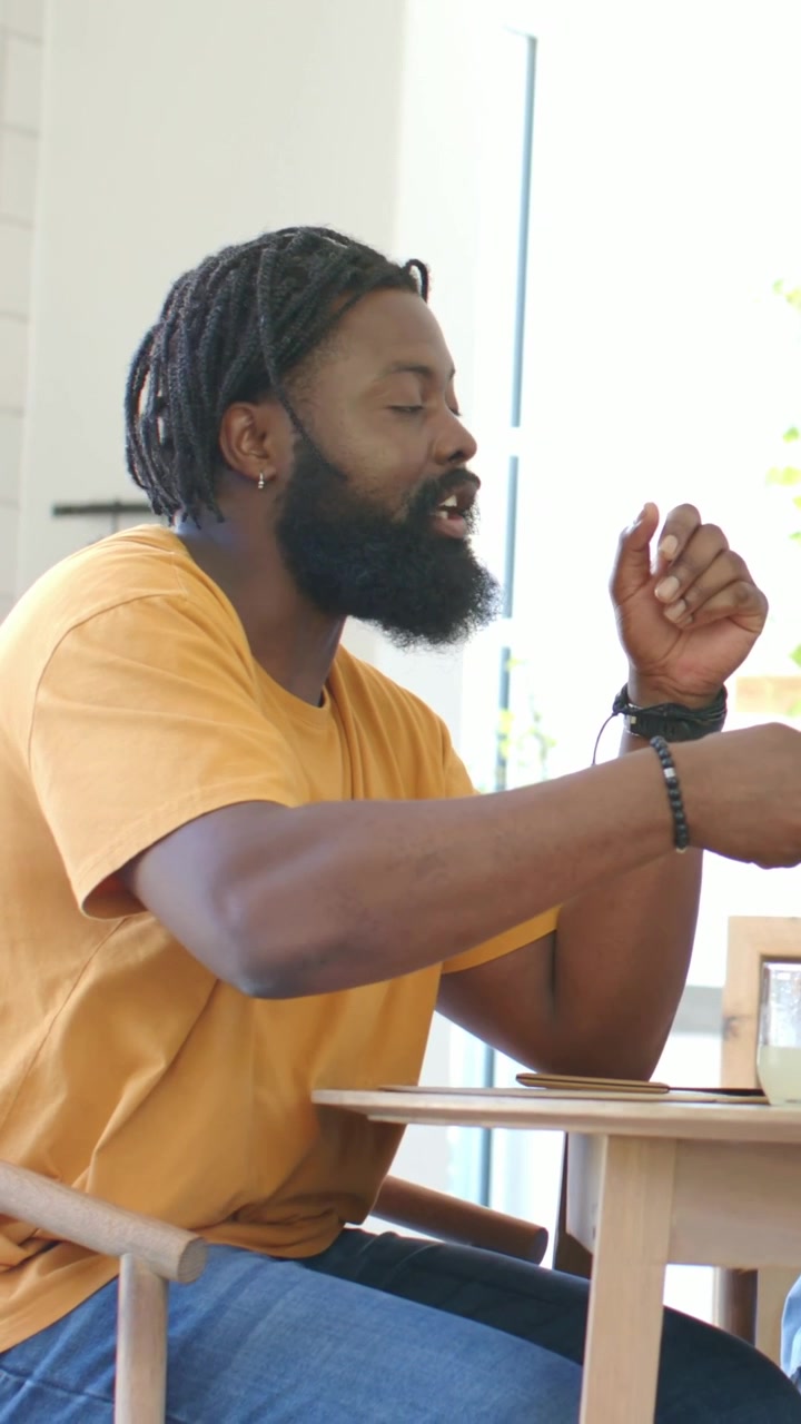 Vertical video: Hearing offscreen prompt man in mustard tee gesturing picking cup at kitchen table