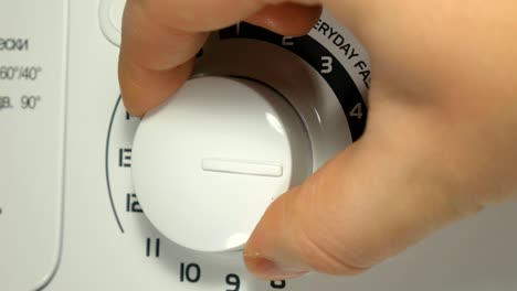 una mano masculina configurando y encendiendo una lavadora electrónica de gama alta.