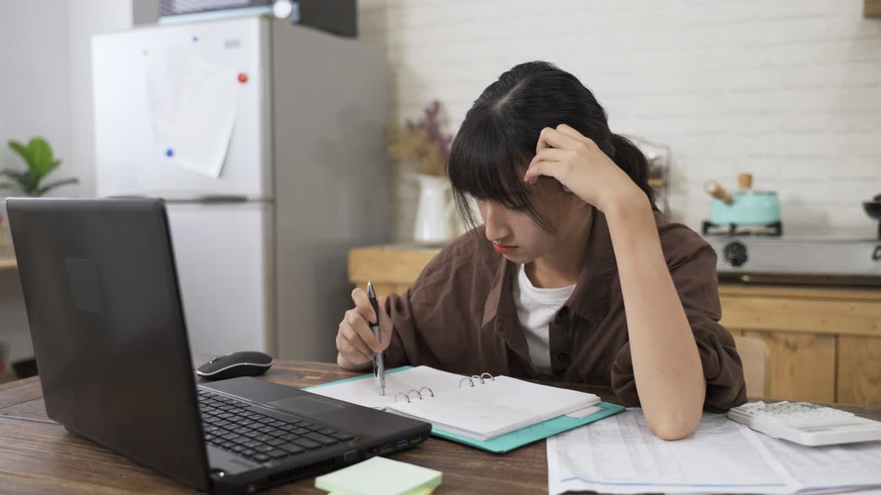 아시아 여성은 펜으로 놀고 노트북을 보고 집에서 식당에서 예산을 계획하는 동안 가정 지불에 대해 걱정하고 있습니다.