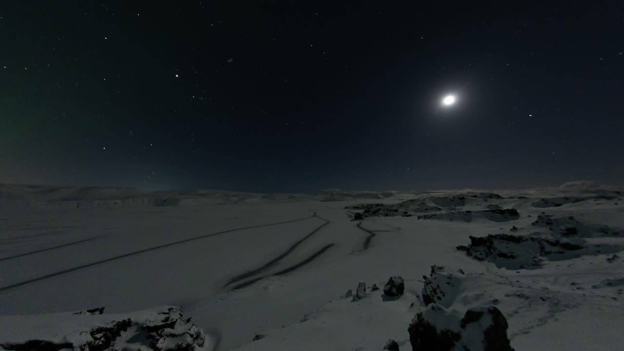 Stabil timelapse med 25 billeder i sekundet, der viser en månebelyst sø med revner i isen i et bjergrigt og vinterligt landskab.