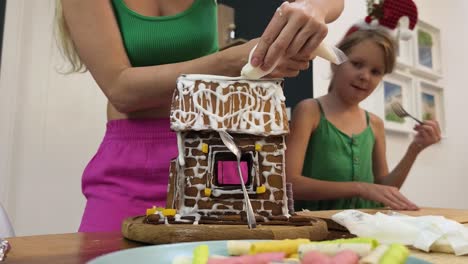 mother and daughter decorating a gingerbread house