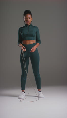 Vertical-Video-Studio-Action-Shot-Of-Female-Athlete-Wearing-Tracksuit-Training-In-Gym-Fitness-Class-With-Jump-Rope-Or-Skipping-Rope-Against-Plain-Background-1