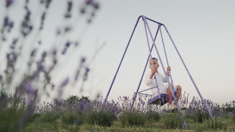 Carefree-boy-rides-on-a-swing-in-a-lavender-field.-Happy-childhood