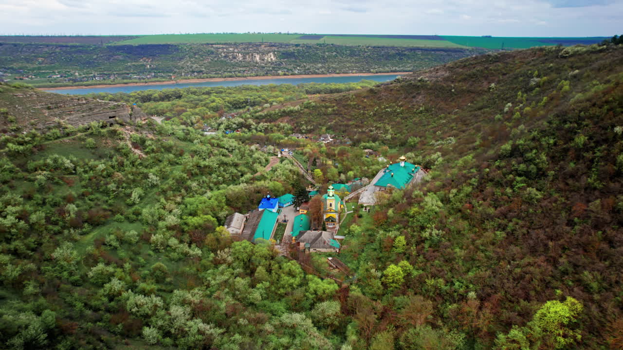Aerial drone view of Saharna Monastery, Moldova. Monastery with churches located in a valley covered with lush forest. Dniester river on the background