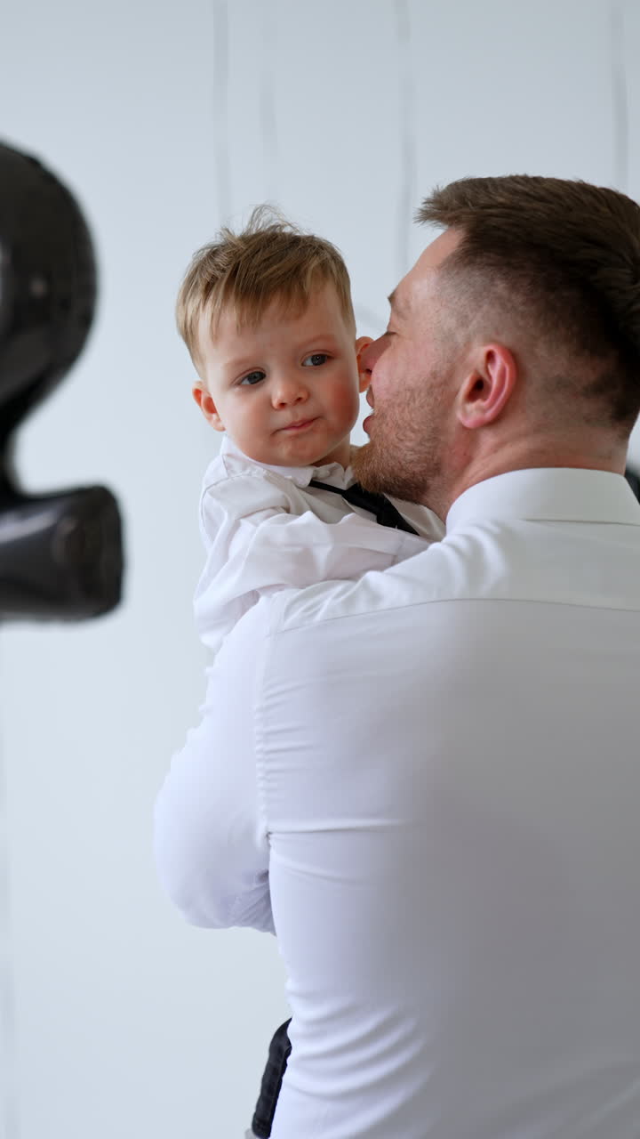 Rear view of a man in white shirt holding a lovely baby boy in his hands. Loving dad kisses his beloved son on the cheek. Vertical video.