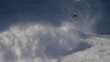 the surfer rides on top of a wave, which throws him into the air and he does a flip over a huge mass of white foamy waves