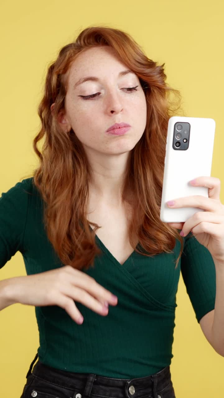 Red-haired woman taking selfies and interacting with her smartphone on a yellow background