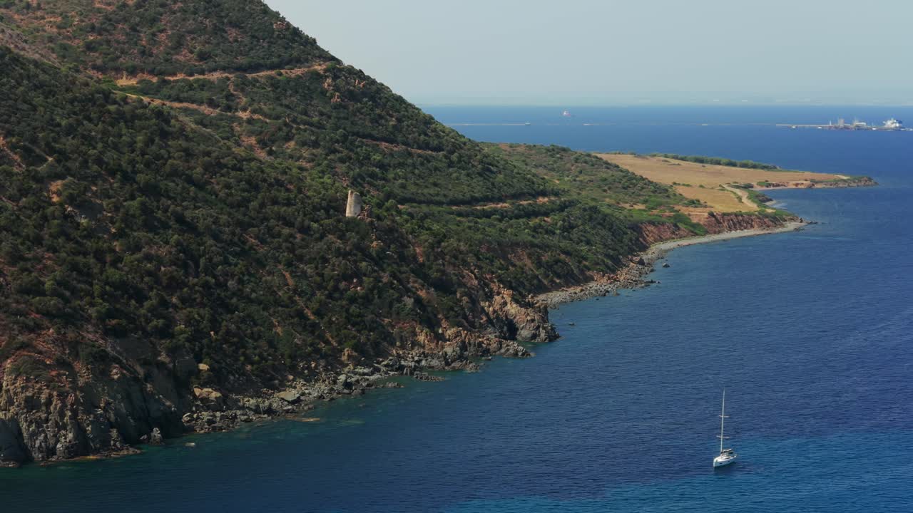Ancient watchtower on rugged, green coast of Sardinia, deep blue Mediterranean Sea, Italy. Aerial drone