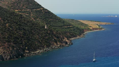 ancient watchtower on rugged, green coast of sardinia, deep blue mediterranean sea, italy. aerial drone