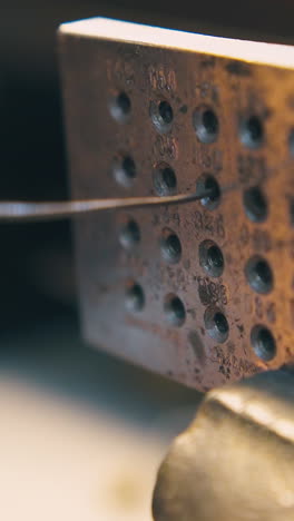 cu: professional goldsmith pulls long gold wire through hole in special tool with pliers in jewelry workshop closeup