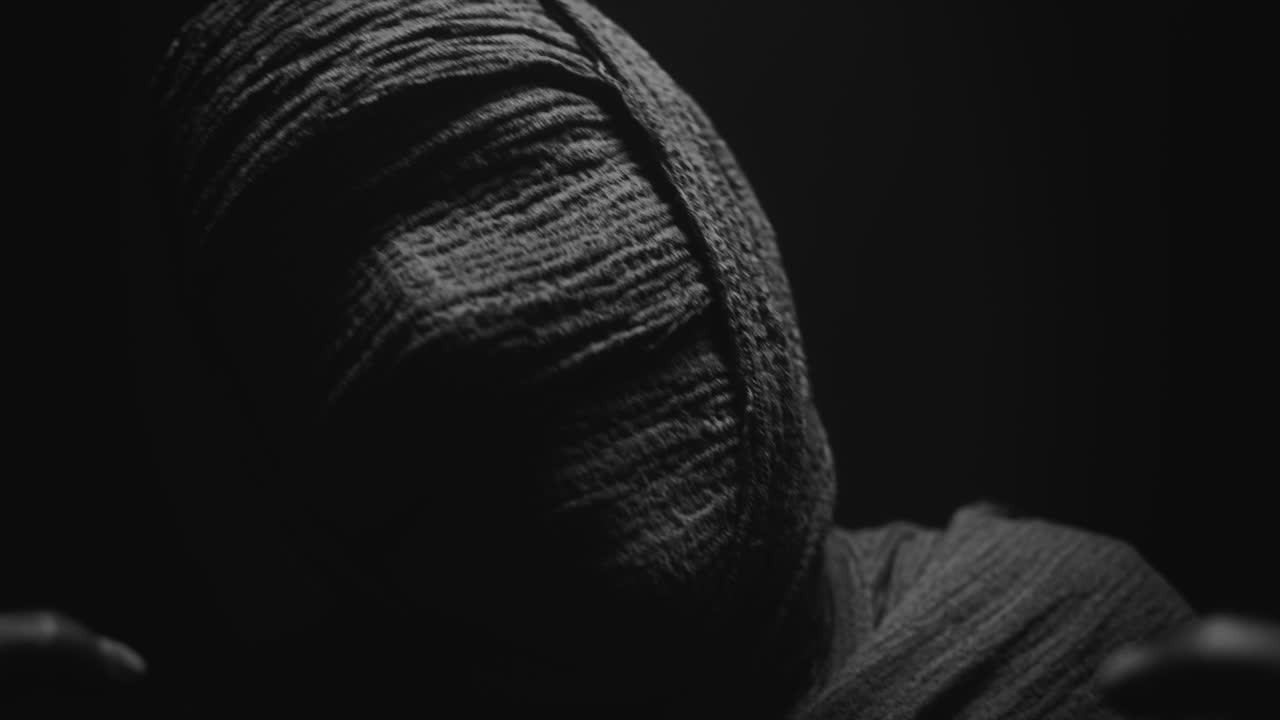 A mummy of a woman on a dark backdrop slowly rises her head