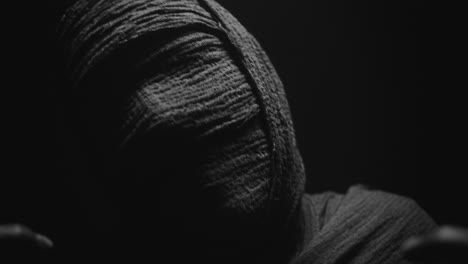 a mummy of a woman on a dark backdrop slowly rises her head