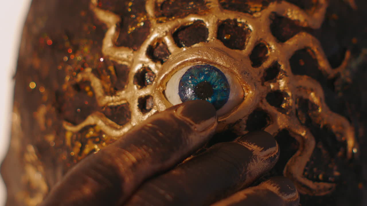 mão pintando uma máscara de olho dourada