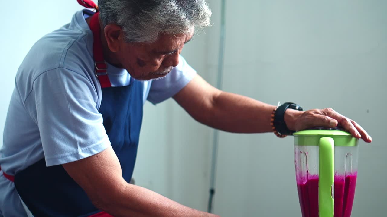Elderly asian man carefully operating blender making pink smoothie