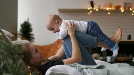 mom plays with baby in white tank top lying on the bed, baby flying and laughing. time lapse of playing together mother and child. flight simulation