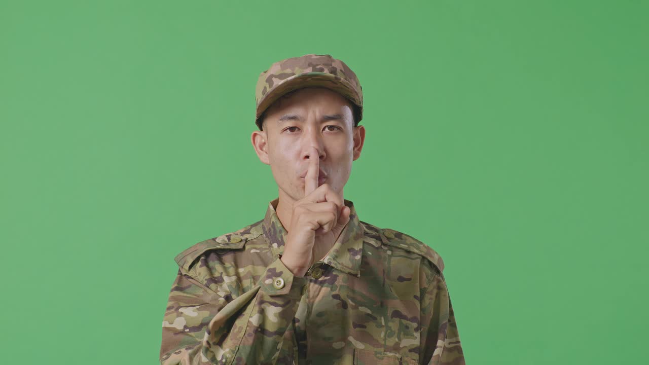 Close Up Of Asian Man Soldier Looking At Camera And Making Shh Gesture While Standing In The Green Screen Background Studio