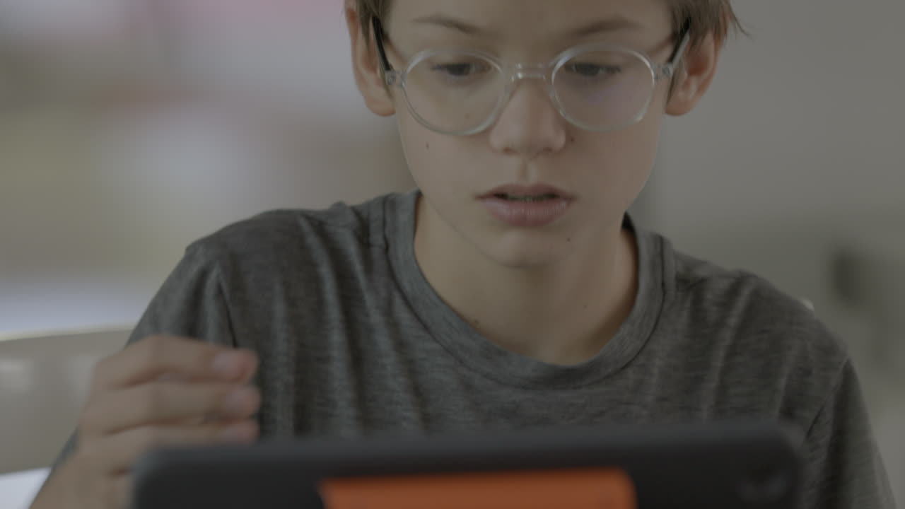 Sød dreng med briller derhjemme, der arbejder på en iPad.