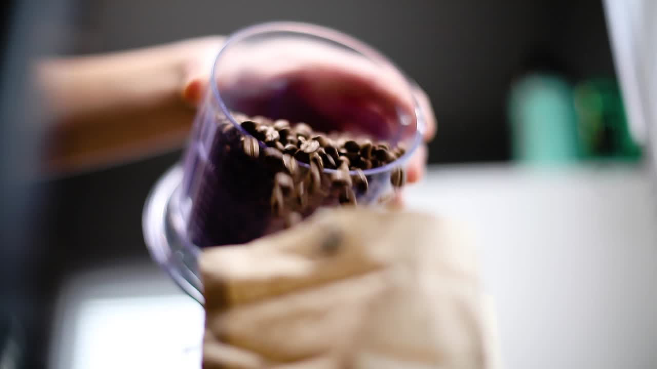 Pouring coffee beans into brown paper bag. Close up slow motion shot. Rack focus
