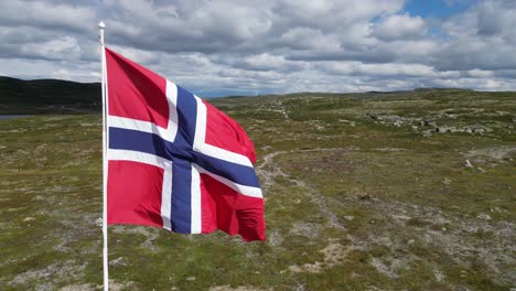 norwegian flag waving in the wind in hardangervidda national park, norway - aerial circling