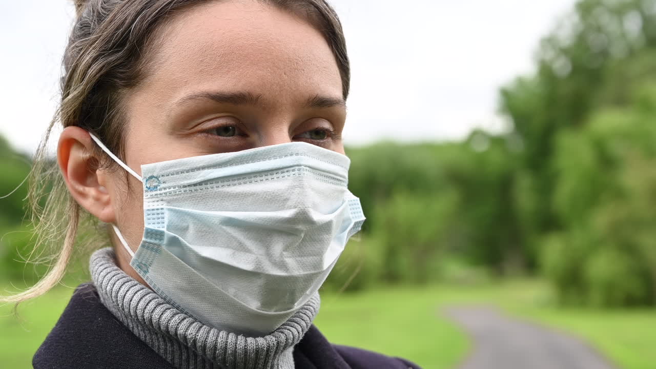 Woman taking off a medical face mask while standing in a park