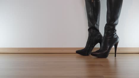 female model in high-heeled black platform leather boots stamps furiously on the floor to destroy something invisible