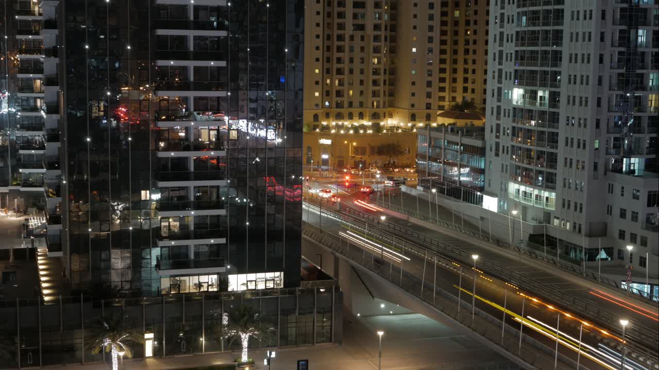 A beautiful time-lapse: nighttime traffic on a busy street in Dubai Marina (residential district in UAE), light streaks from cars reflecting on the glass surfaces of skyscrapers.