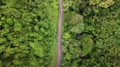 Aerial-top-view-of-remote-road-with-motorcyclist-over-top-of-mountain-with-green-jungle-in-Sumbawa-Island,-Indonesia