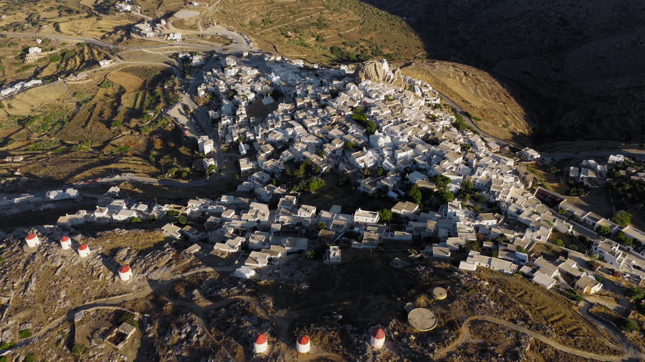 Aerial establishing shot of Chora town whitewashed houses, Venetian fortress castle, traditional windmills at sunrise, Aegean sea, Amorgos island