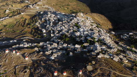 aerial establishing shot of chora town whitewashed houses, venetian fortress castle, traditional windmills at sunrise, aegean sea, amorgos island