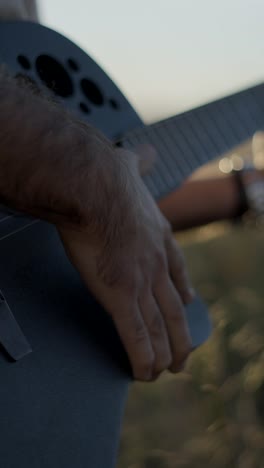 person playing acoustic guitar outdoors at sunset