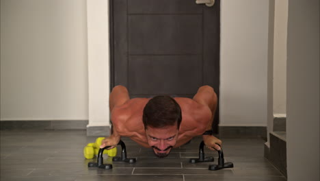 slow motion front view of a latin hispanic fit man training at home doing push ups using helping support bars